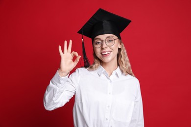 Photo of Happy student showing ok gesture after graduation on red background