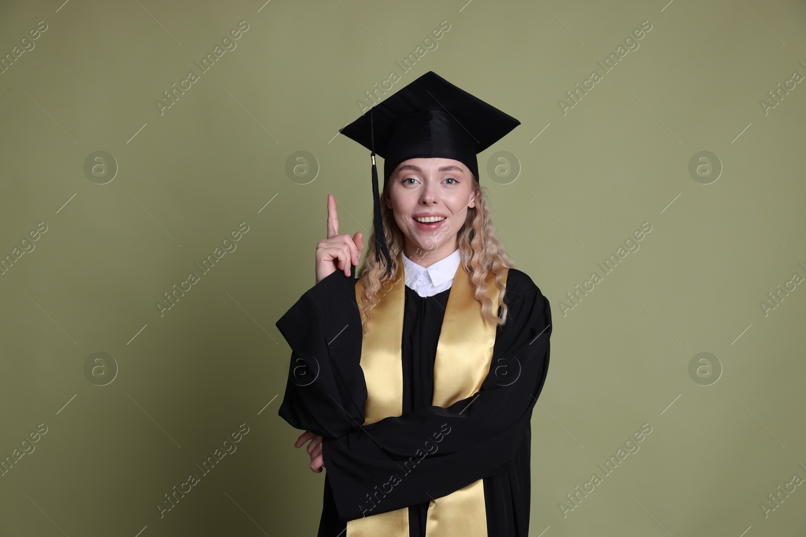 Happy student pointing upwards after graduation on green background Photo of Happy student pointing upwards after graduation on green background