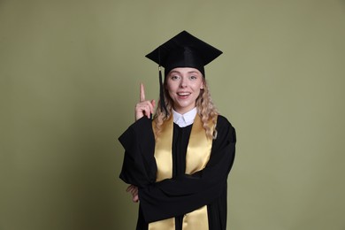 Photo of Happy student pointing upwards after graduation on green background
