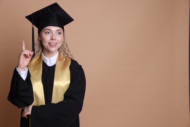 Photo of Happy student pointing upwards after graduation on beige background. Space for text