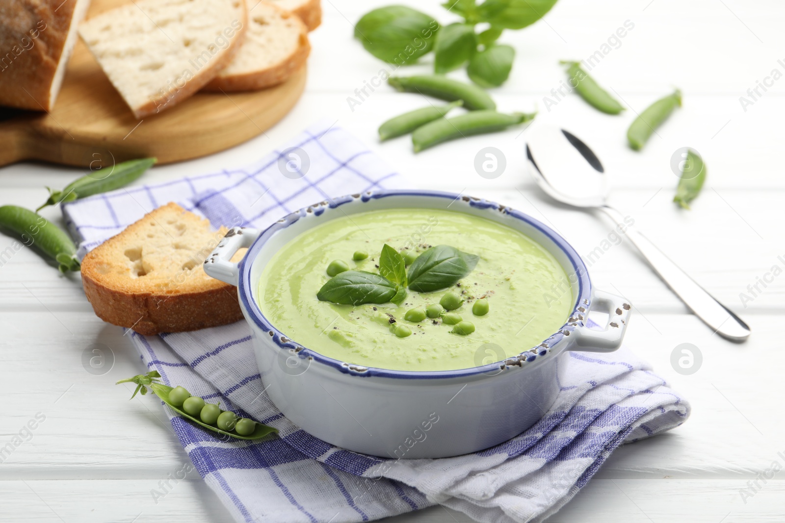 Tasty pea cream soup with basil served on white wooden table Photo of Tasty pea cream soup with basil served on white wooden table