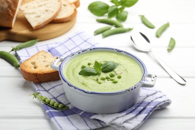 Photo of Tasty pea cream soup with basil served on white wooden table