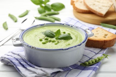 Photo of Tasty pea cream soup with basil served on white wooden table, closeup