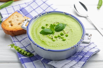 Photo of Tasty pea cream soup with basil served on white wooden table, closeup