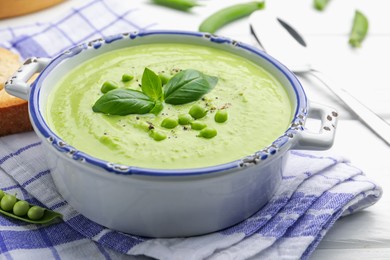 Photo of Tasty pea cream soup with basil served on white wooden table, closeup