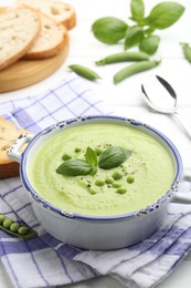 Photo of Tasty pea cream soup with basil served on white table