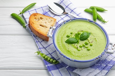 Photo of Tasty pea cream soup with basil served on white wooden table, closeup