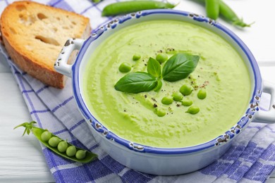 Photo of Tasty pea cream soup with basil served on white wooden table, closeup