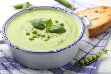 Photo of Tasty pea cream soup with basil served on white wooden table, closeup