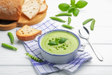 Photo of Tasty pea cream soup with basil served on white wooden table