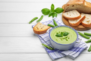 Photo of Tasty pea cream soup with basil served on white wooden table. Space for text