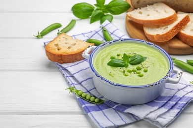 Photo of Tasty pea cream soup with basil served on white wooden table