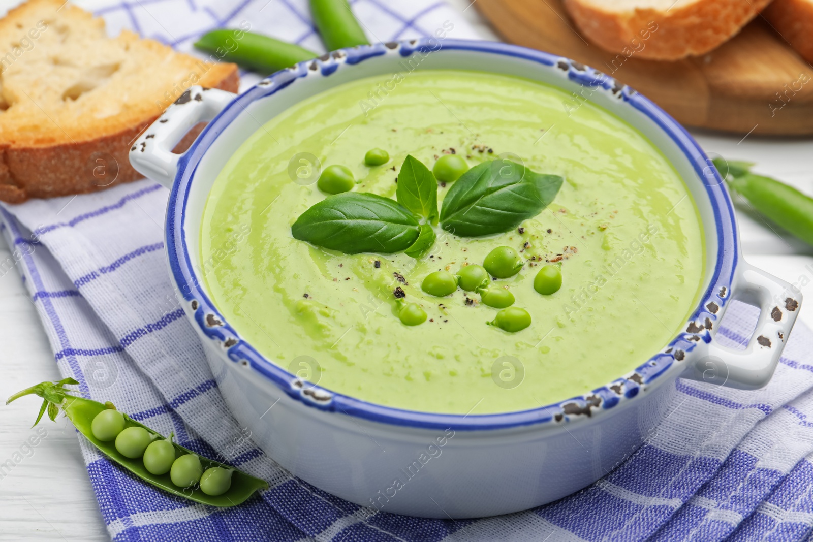 Tasty pea cream soup with basil served on white wooden table, closeup Photo of Tasty pea cream soup with basil served on white wooden table, closeup