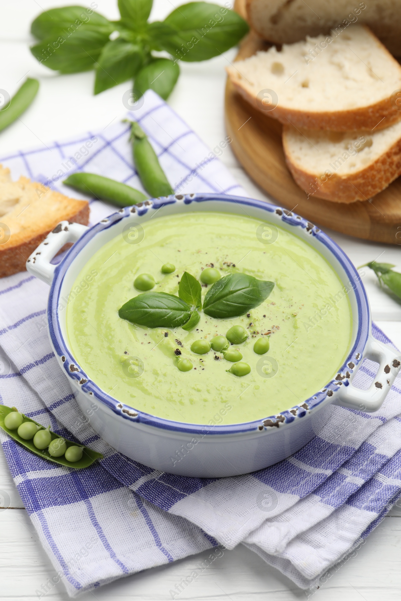 Photo of Tasty pea cream soup with basil served on white wooden table