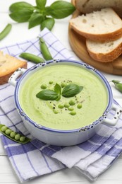 Photo of Tasty pea cream soup with basil served on white wooden table