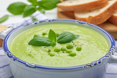 Photo of Tasty pea cream soup with basil served on table, closeup