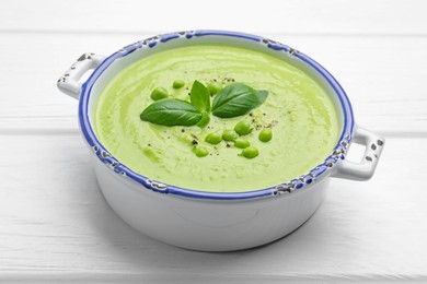 Photo of Tasty pea cream soup with basil on white wooden table, closeup