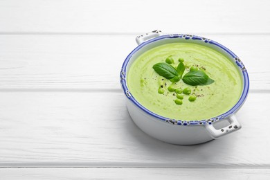 Photo of Tasty pea cream soup with basil on white wooden table. Space for text