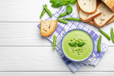 Photo of Tasty pea cream soup with basil served on white wooden table, flat lay. Space for text