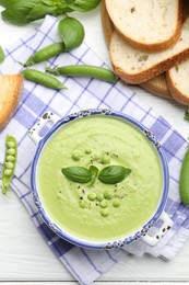 Photo of Tasty pea cream soup with basil served on white wooden table, flat lay
