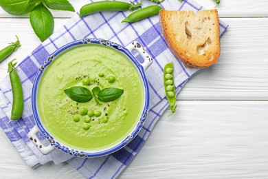 Photo of Tasty pea cream soup with basil served on white wooden table, flat lay