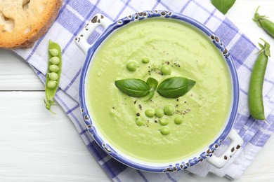Photo of Tasty pea cream soup with basil served on white wooden table, flat lay
