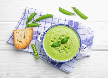 Photo of Tasty pea cream soup with basil served on white wooden table, flat lay