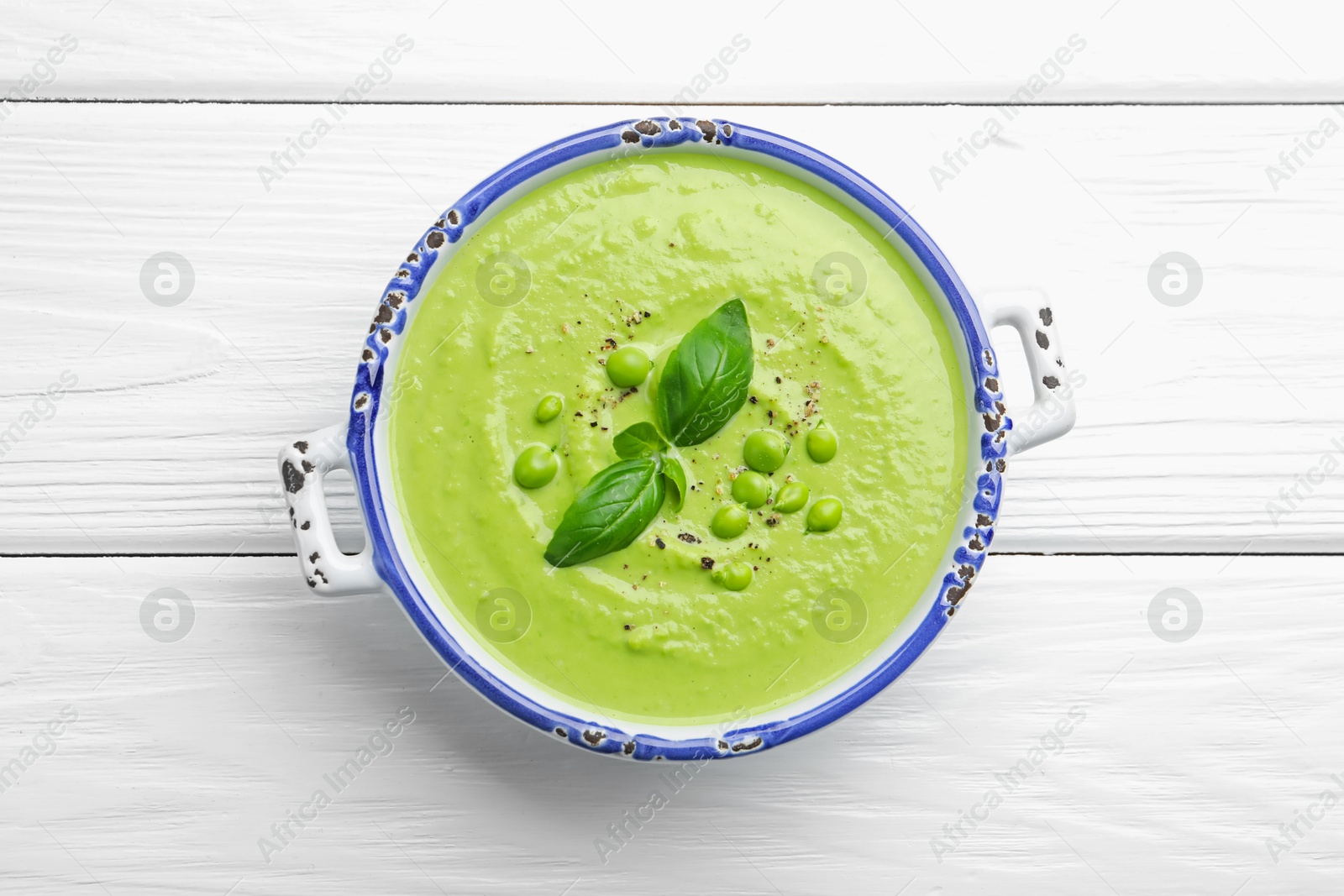 Tasty pea cream soup with basil on white wooden table, top view Photo of Tasty pea cream soup with basil on white wooden table, top view