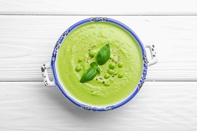 Photo of Tasty pea cream soup with basil on white wooden table, top view