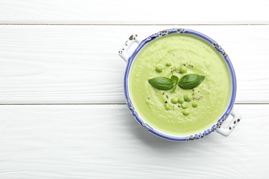 Photo of Tasty pea cream soup with basil on white wooden table, top view. Space for text