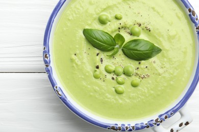 Photo of Tasty pea cream soup with basil on white wooden table, top view