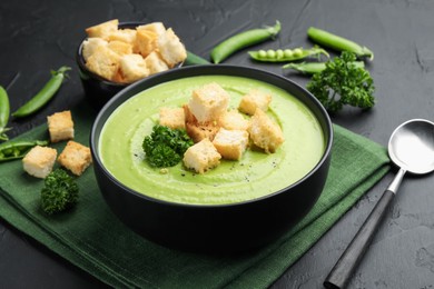 Photo of Tasty pea cream soup with croutons and broccoli served on black table, closeup