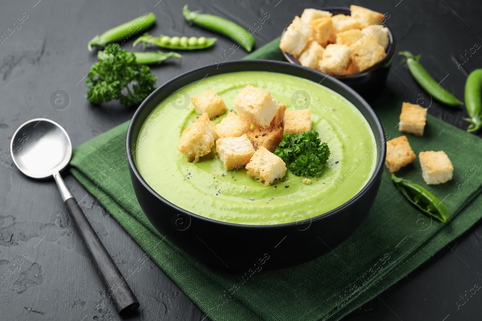 Photo of Tasty pea cream soup with croutons and broccoli served on black table, closeup