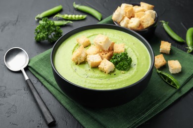 Photo of Tasty pea cream soup with croutons and broccoli served on black table, closeup