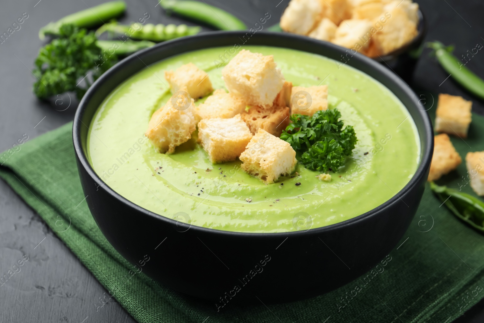 Photo of Tasty pea cream soup with croutons and broccoli served on black table, closeup