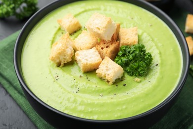 Photo of Tasty pea cream soup with croutons and broccoli served on black table, closeup