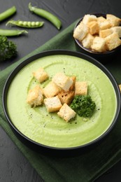 Photo of Tasty pea cream soup with croutons and broccoli served on black table, closeup