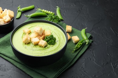 Photo of Tasty pea cream soup with croutons and broccoli served on black table, closeup. Space for text