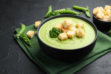 Photo of Tasty pea cream soup with croutons and broccoli served on black table, closeup