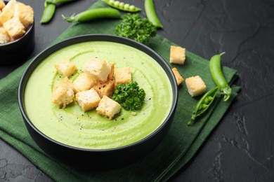 Photo of Tasty pea cream soup with croutons and broccoli served on black table, closeup