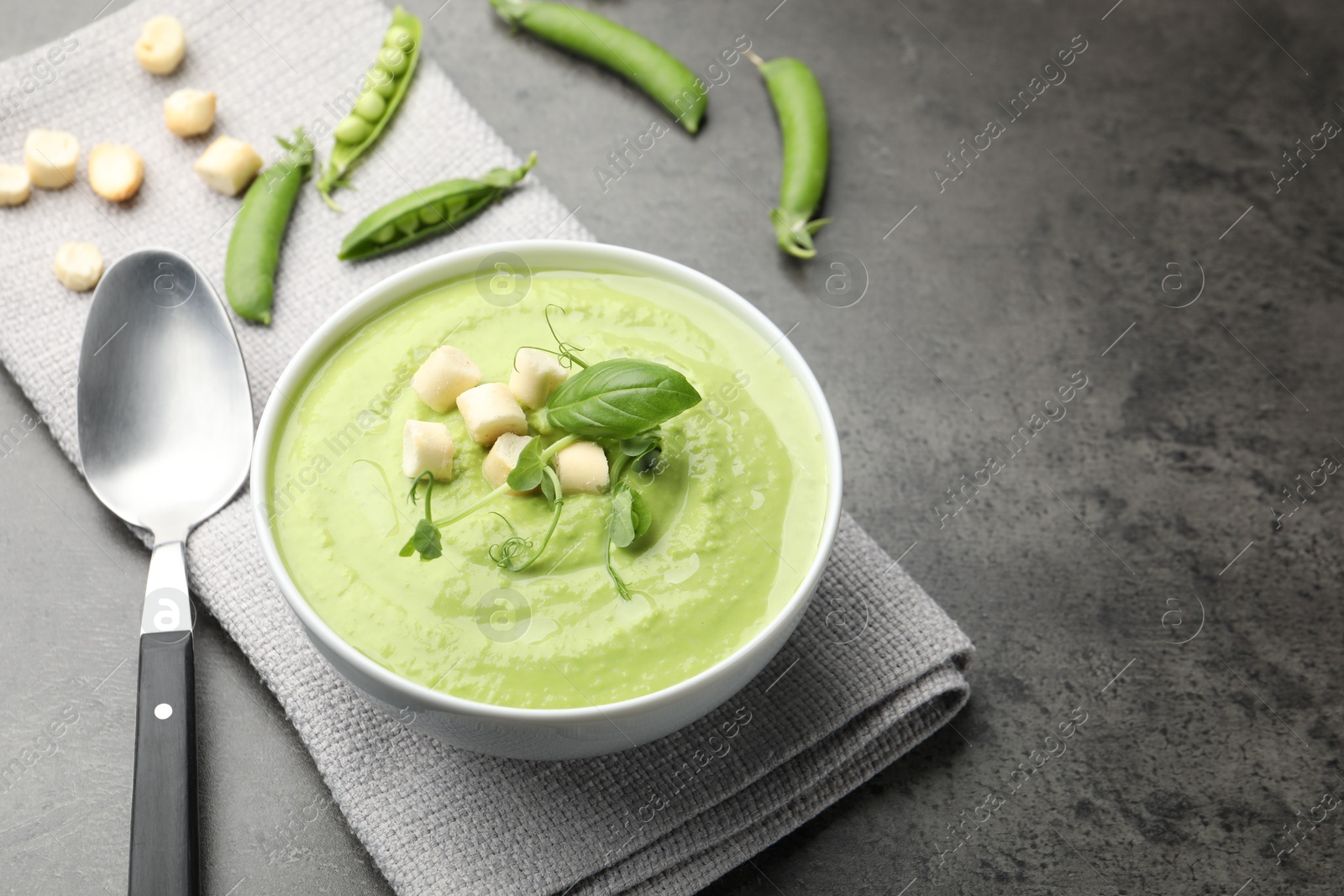 Photo of Tasty pea cream soup with croutons, basil and microgreens served on grey table. Space for text
