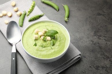 Photo of Tasty pea cream soup with croutons, basil and microgreens served on grey table. Space for text