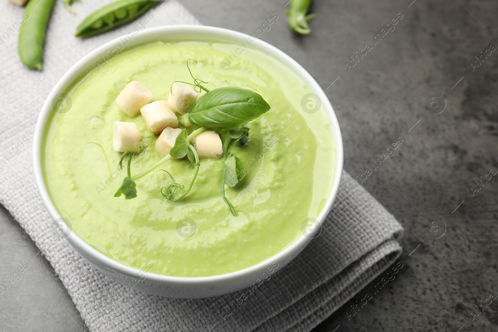 Tasty pea cream soup with croutons, basil and microgreens served on grey table, closeup Photo of Tasty pea cream soup with croutons, basil and microgreens served on grey table, closeup