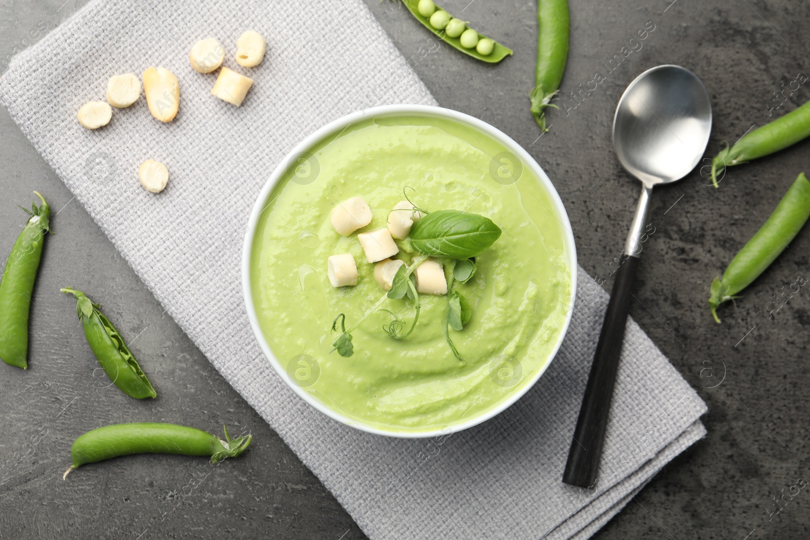 Photo of Tasty pea cream soup with croutons, basil and microgreens served on grey table, flat lay