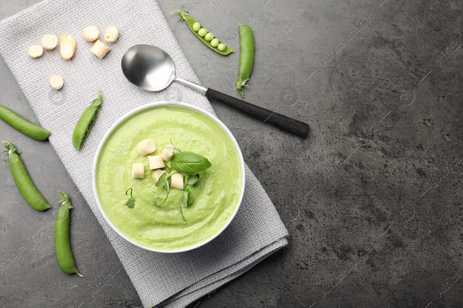 Tasty pea cream soup with croutons, basil and microgreens served on grey table, flat lay. Space for text Photo of Tasty pea cream soup with croutons, basil and microgreens served on grey table, flat lay. Space for text