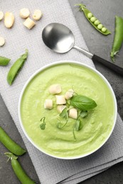 Photo of Tasty pea cream soup with croutons, basil and microgreens served on grey table, flat lay