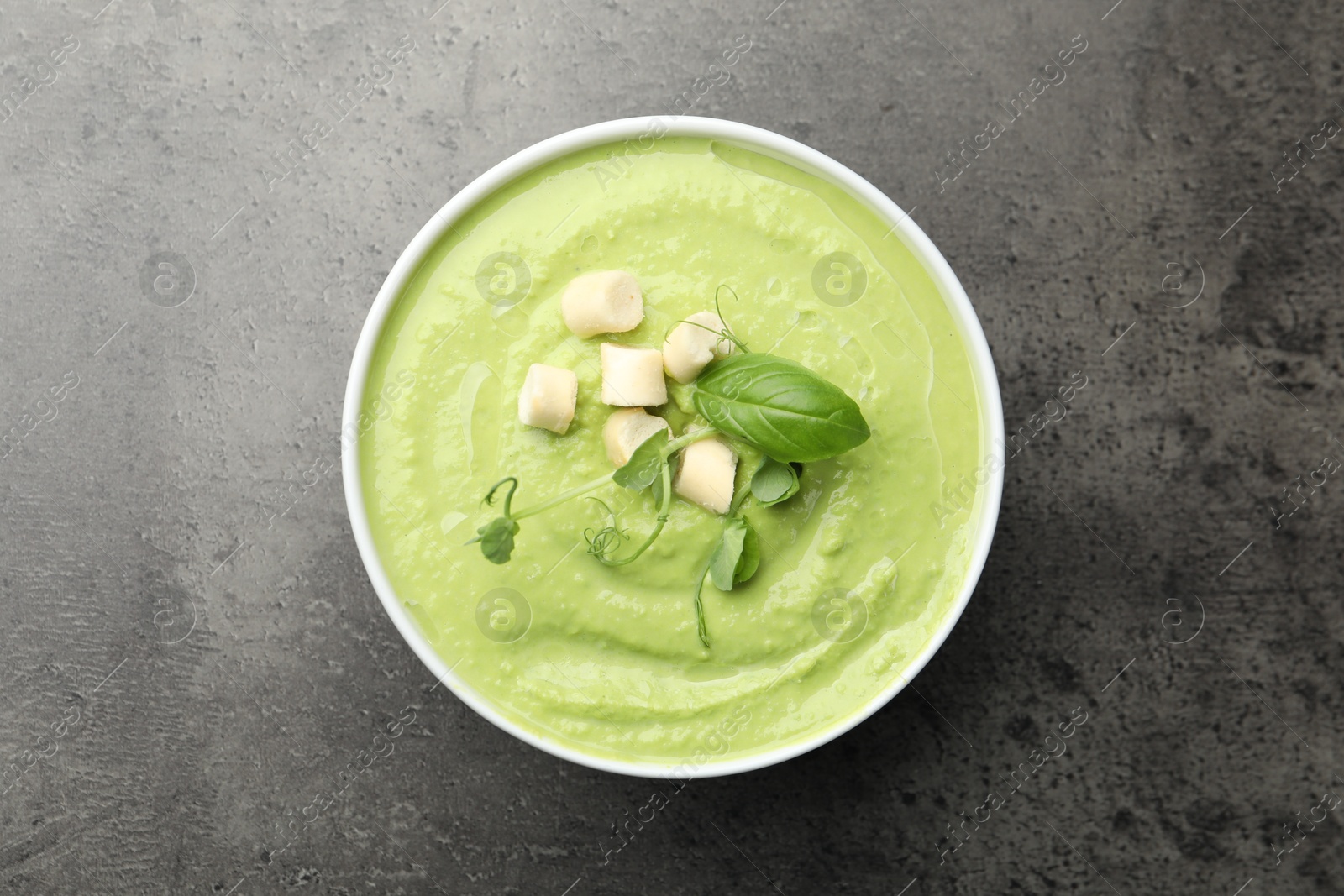 Tasty pea cream soup with croutons, basil and microgreens on grey table, top view Photo of Tasty pea cream soup with croutons, basil and microgreens on grey table, top view
