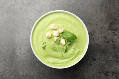 Photo of Tasty pea cream soup with croutons, basil and microgreens on grey table, top view