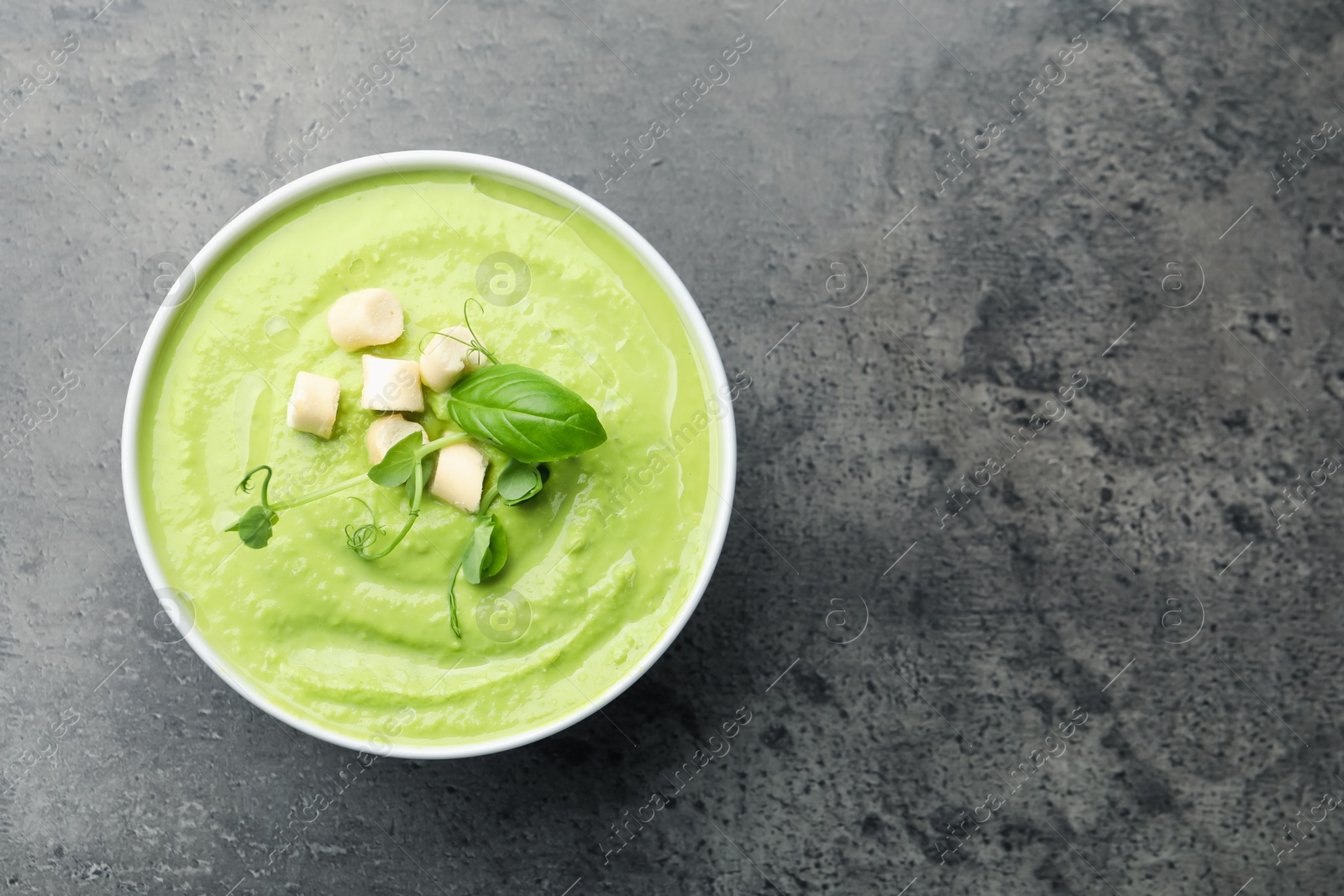 Tasty pea cream soup with croutons, basil and microgreens on grey table, top view. Space for text Photo of Tasty pea cream soup with croutons, basil and microgreens on grey table, top view. Space for text