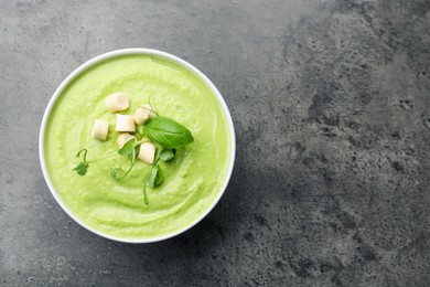 Photo of Tasty pea cream soup with croutons, basil and microgreens on grey table, top view. Space for text